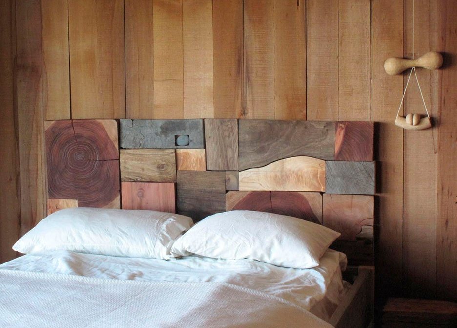 A bed beneath a headboard of assembled wood blocks by JB Blunk, against a plank wall