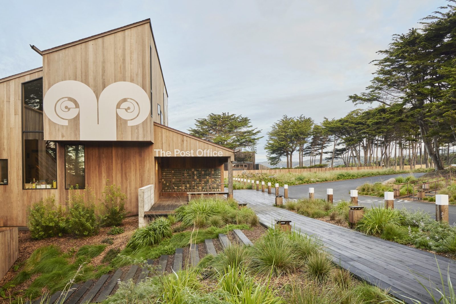 The Sea Ranch post office, a timber building marked with the ram supergraphic beside a boardwalk through native planting