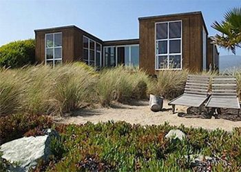 A low wood-clad beach house set among dune grass and coastal scrub