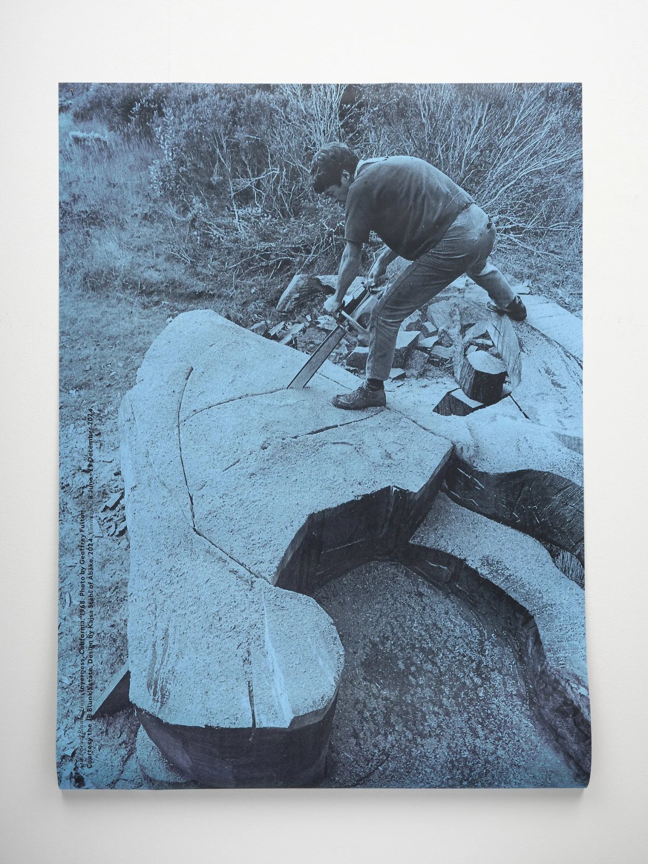 A blue-toned photograph of JB Blunk carving a large stone on a hillside