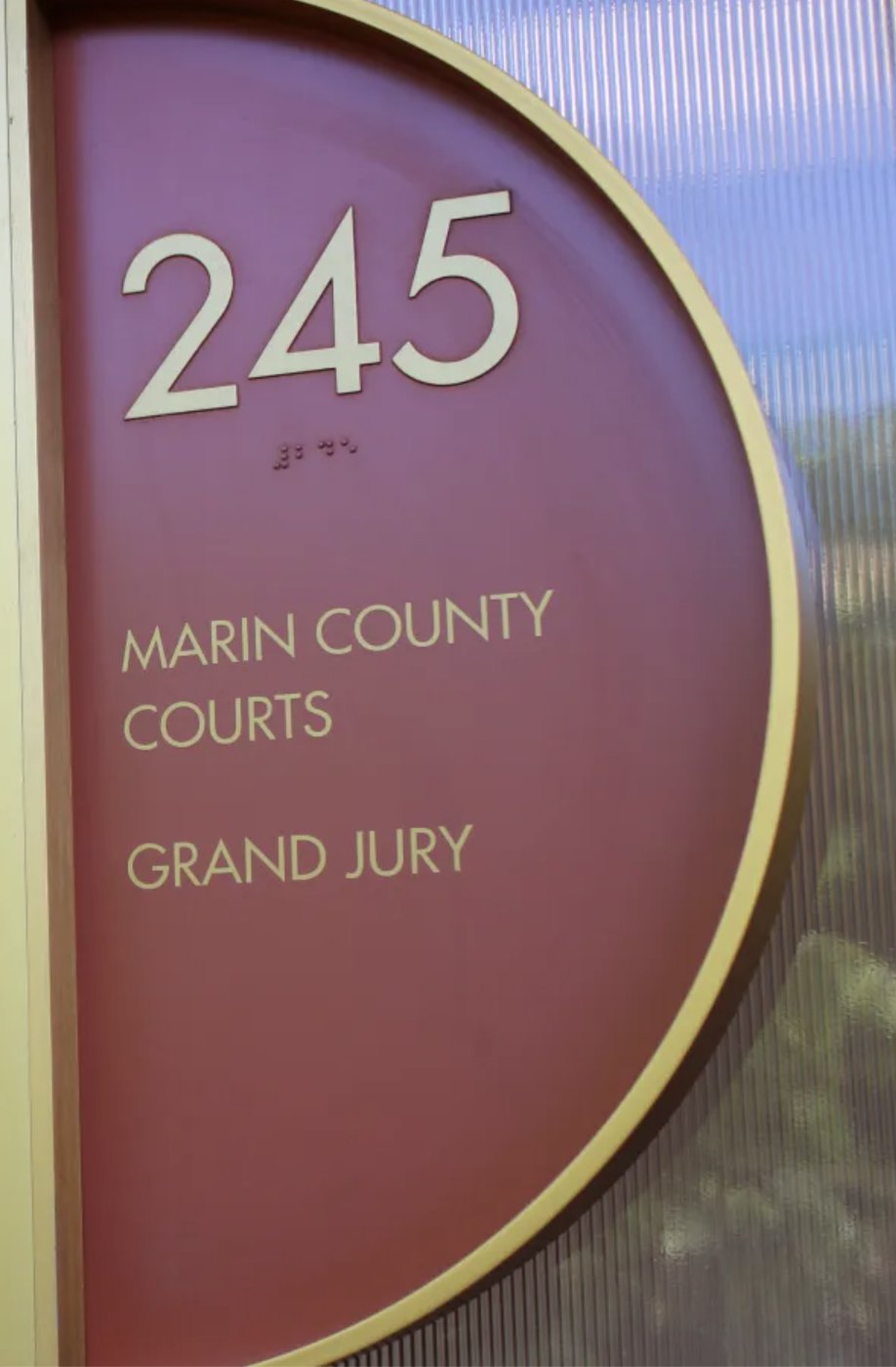 A curved sign at the Marin County Civic Center in rose and gold, reading 245, Marin County Courts, Grand Jury, with braille set beneath the number