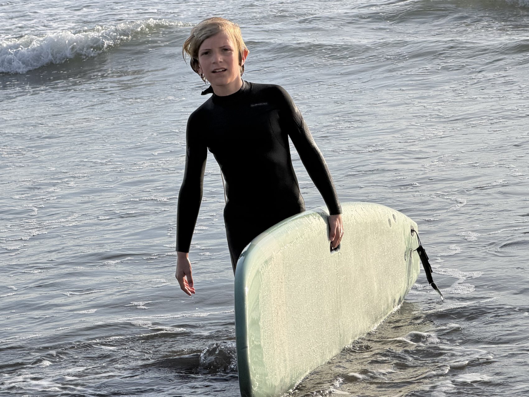 A young surfer holding a surfboard on the beach