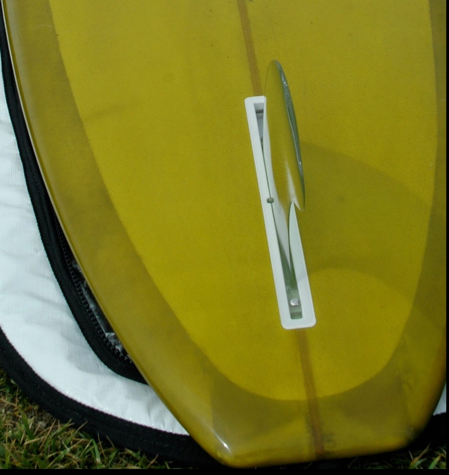 The tail of a kelp-tinted Junod longboard with a clear single fin in its box