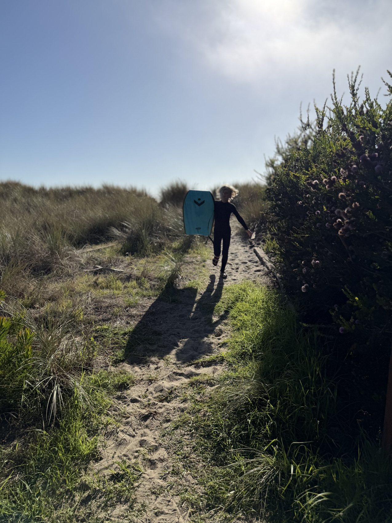 Walking up a sandy path from the beach carrying a surfboard